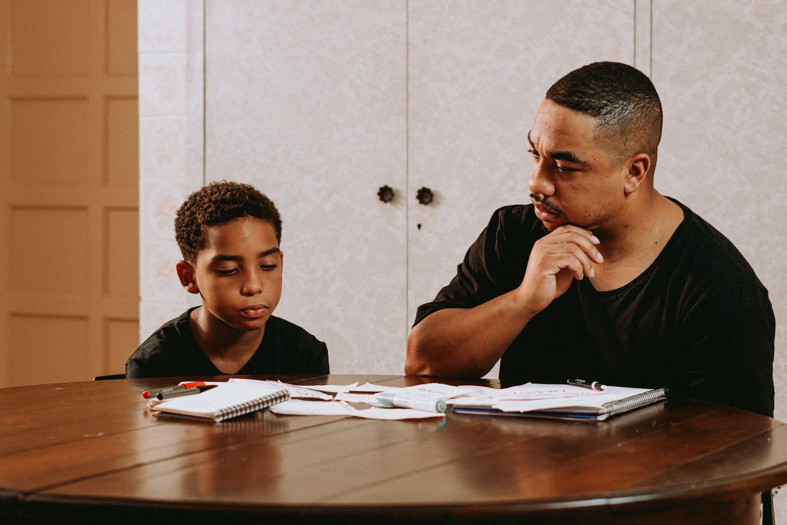 A father and son working through schoolwork together at the kitchen table